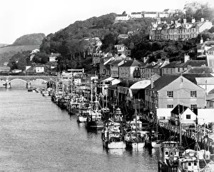 Impressions de Une vue de l'air de Looe en Cornouailles montrant des bateaux à pêche, le quai et un pont ainsi que diverses constructions s'étendant vers la colline au loin Looe Impressions: Vue aérienne de Looe en Cornouailles