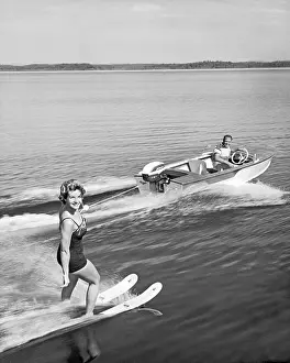 États-Unis : c. 1958 Une femme jolie sourit à la caméra alors quelle tient avec une main tout en ski nautique sur un lac.