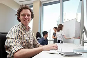 Office Communication Skills Impressions: Young man using computer in office looking towards camera