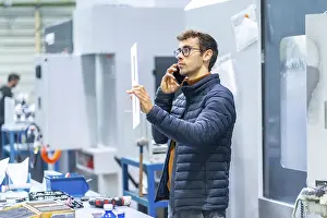 Communicative Young Adult Man Impressions: Engineer talking to the mobile in a computer numeric control factory