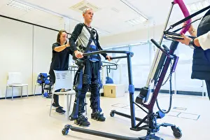 Physical Therapy Exercises Impressions: Mechanical exoskeleton. Female physiotherapy medical assistant lifting disabled person with robotic skeleton