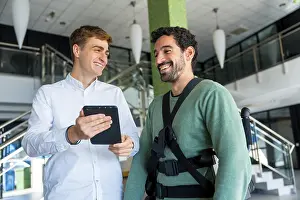 Physical Therapy Treatment Impressions: Mechanical exoskeleton, physiotherapist looking at consultation with tablet with disabled person with robotic skeleton