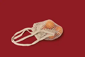 Single Colored Background Photo Impressions: Oranges in a string bag on ruby red background