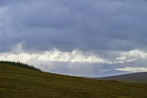 Scottish Highland Landscapes Impressions: Rays of light break through the clouds above a hill with trees
