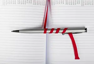 Office Supply Desk Utensils Impressions: Silver pen on opened notebook with red string