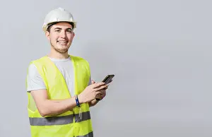 Young Engineer Impressions: Smiling engineer using cell phone looking at camera