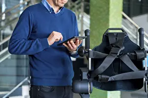 Physiotherapy Robot Impressions: Unrecognizable computer engineer in mechanical exoskeleton looking at the robot with a tablet